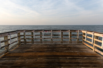 Wooden Pier Facing Ocean Horizon. A weathered wooden fishing pier stretches over the ocean under a...