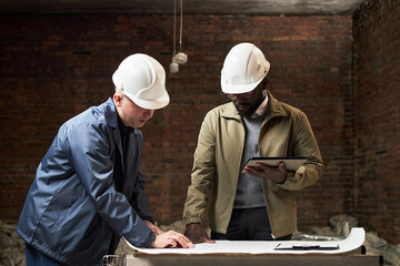 Medium shot of professional builders with white helmet looking at office plan and editing it together
