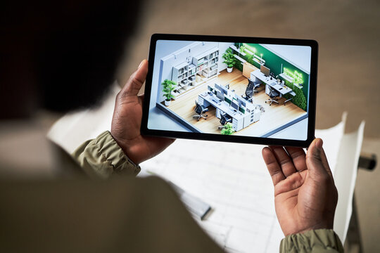 Over shoulder view of unrecognizable foreman holding black tablet with layout plan of IT office on screen