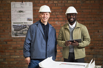 Portrait of African American designer of interior with tablet in hand and Caucasian foreman smiling...