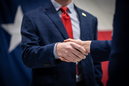 Male and Female Business Professionals or Politicians In Suits Shaking Hands In Front of the Texas Flag Close Up