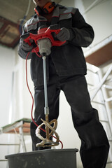 Low angle shot dirty drill mixer in hand of professional worker, he taking it from dirty plastic bucket full of cement