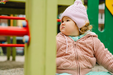 A young child wearing a knitted hat and cozy sweater explores a vibrant playground The setting features bright colors and a cheerful atmosphere perfect for outdoor fun