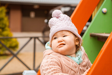 A young child wearing a knitted hat and cozy sweater explores a vibrant playground The setting features bright colors and a cheerful atmosphere perfect for outdoor fun