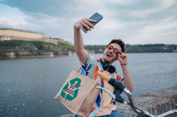 Young tourist taking selfie while promoting sustainable tourism with reusable bag