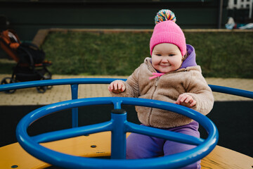 Child Enjoys Spinning on Playground Equipment in Vibrant Winter Attire During Sunny Afternoon