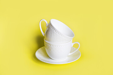a tower of white beautiful tea cups with a pattern on a white saucer stands neatly on a yellow background in the center, two cups one on top of the other