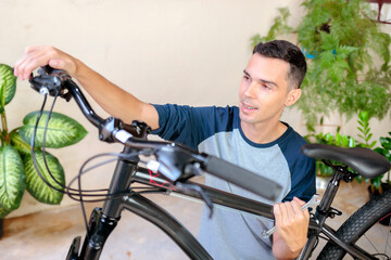 Obraz premium Brazilian man checking the brakes and handlebar alignment of a mountain bike. Concept of bike safety, home maintenance, and preparation before riding