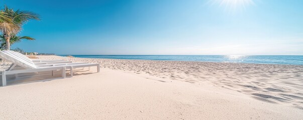 A serene beach scene featuring white sand, inviting lounge chairs, and a clear blue sky reflecting the sun"s rays over calm ocean waters.
