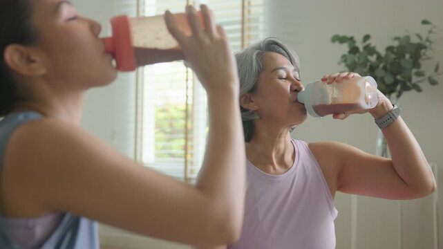 Young adult child active mature middle age old mum drink whey protein shake bottle diet food after home workout. Love health care older aged mom asia elder people happy relax sport protect aging life.