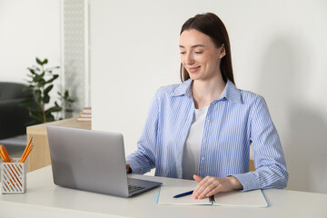 Smiling woman learning online using laptop at table indoors. Self-study