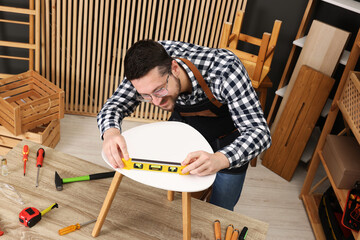 Relaxing hobby. Man using level tool while repairing stool at wooden table in workshop