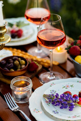 Beautiful elegant romantic dinner table decor, surprise day arrangement. Marriage proposal, engagement private party for two in a meadow. Sunset, golden hour. Cheese board, rose wine, fruits, lupine