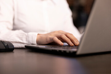 A closeup of a woman typing on her laptop, her fingers swiftly navigating the keyboard as she inputs financial data. The selective focus draws attention to her hands in a modern office.