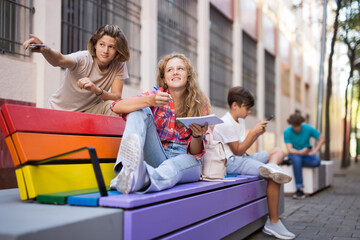 Guy and girl have fun chatting on bench. Guy points his hand at someone