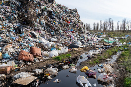 A large pile of waste fills the landscape, with plastic bags and other debris strewn across both the ground and the adjacent muddy road
