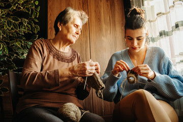 Senior caucasian woman teach granddaughter how to knit with needles 