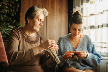 Senior caucasian woman teach granddaughter how to knit with needles 