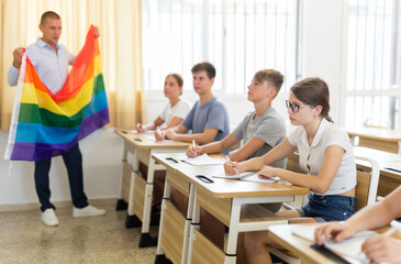 School teacher with flag explains to students what is LGBT in schoolroom