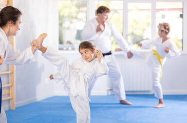 Focused preteen girl in white kimono practicing karate kicking techniques during sparring with...