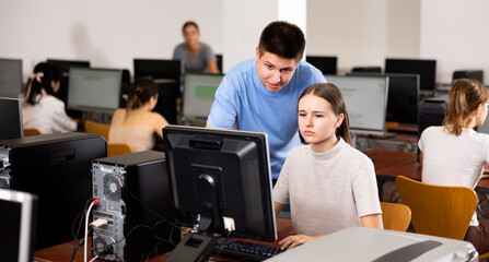 Fototapeta premium Focused boy helping young female student working with pc in library computer room