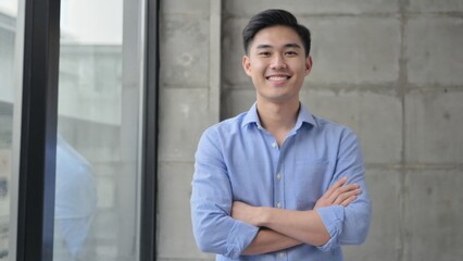 Obraz premium Portrait of a young man with a confident smile and relaxed posture, standing in an office environment.
