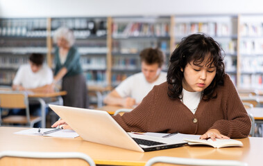 Asian teenager girl with a laptop studying in the school library