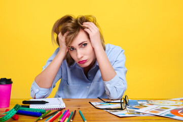 stressed woman in blue shirt working at cluttered desk filled with colorful stationery and...