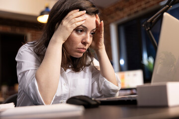 Exhausted caucasian manager holding her head, looking at laptop, showing signs of fatigue. Closeup...