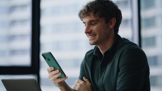 Worker receiving cellphone salary notification working at laptop office closeup.