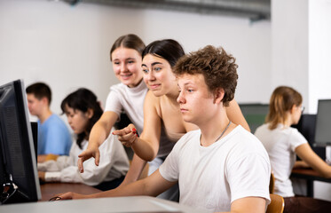 Positive young boy and girls using personal computer together. Cheerful teenagers in computer class.