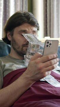 Man make money online, tapping smartphone screen. Money rain flow through the smartphone. Cash flow, dollar bills floating in the man face. Online winning. Business making easy money online concept