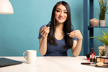 Asian makeup artist with a mascara in her hand, shooting a tutorial video for her online audience....