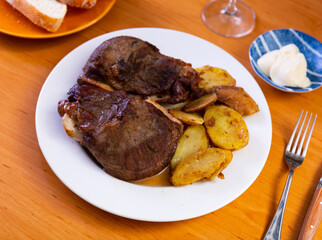 Appetizing roasted pork cheeks served with vegetable garnish of baked potatoes and spicy creamy sauce