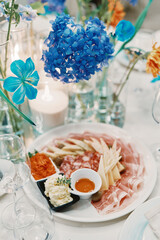 Sliced meats with pieces of cheese lie on a plate on a set table