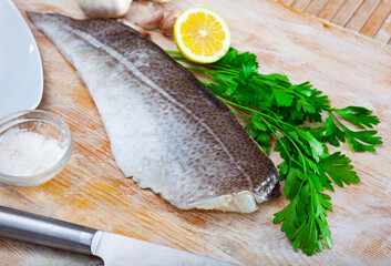 Raw codfish fillet lying on wooden table with condiments. Cooking ingredients