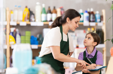 Woman seller with daughter, make inventory using paper report in store. Little girl helps her mother during inventory, learns trading skills