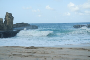 Just beyond the shore, waves crash energetically against the rocky formations jutting out from the sea