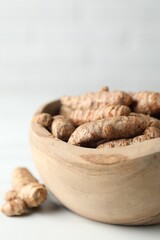 Raw turmeric roots in bowl on white table, closeup