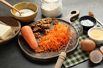 Different ingredients for making carrot cake and whisk on dark textured table, closeup