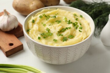 Tasty mashed potato with green onion in bowl on white table, closeup