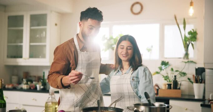 Couple, cooking and taste food in kitchen with meal preparation, helping and nutrition lunch. Embrace, man and feeding woman for healthy ingredients, test gourmet cuisine and bonding together at home