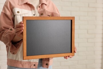 Woman holding blank small blackboard indoors, closeup