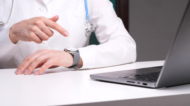 Doctor pointing at wristwatch near laptop at clinic