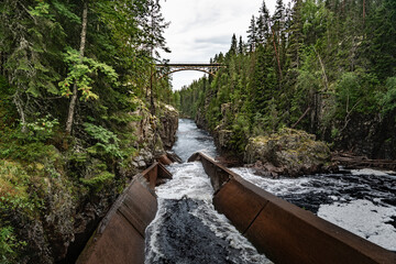 A railway bridge arches over the deep canyon of Storstupet, with rushing waters of the River Ämån...