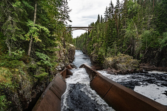 A railway bridge arches over the deep canyon of Storstupet, with rushing waters of the River &Auml;m&aring;n below, surrounded by dense trees a log flume in a rugged terrain in Orsa Dalarna