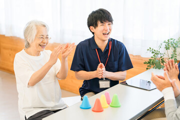 リハビリ施設,介護施設で働く若いアジア人男性スタッフとシニア女性
