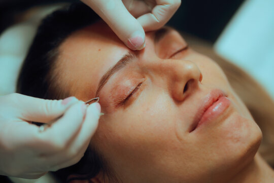Beautician Tweezing Excess Eyebrow Hair of a Happy Client. happy client at a beauty salon getting her eyebrows done
