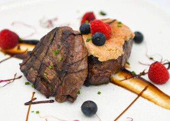 Postre con crema, frutos rojos y salsa de chocolate sobre fondo blanco.