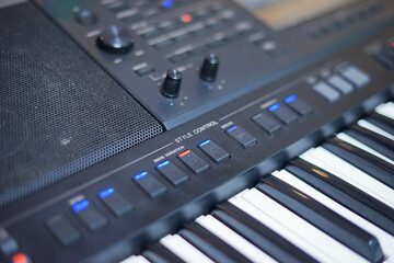 Close-up of an electronic keyboard showing style control buttons, volume knobs, speaker grill, and black and white piano keys, perfect for a music and studio concept.